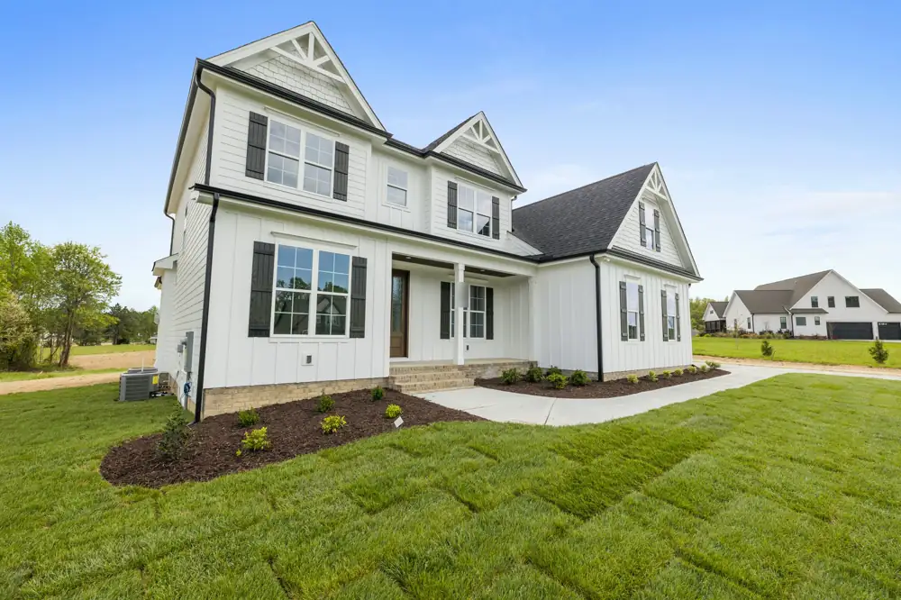 A white board-and-batten farmhouse with black windows and shutters, gabled front and a fresh lawn in the foreground.